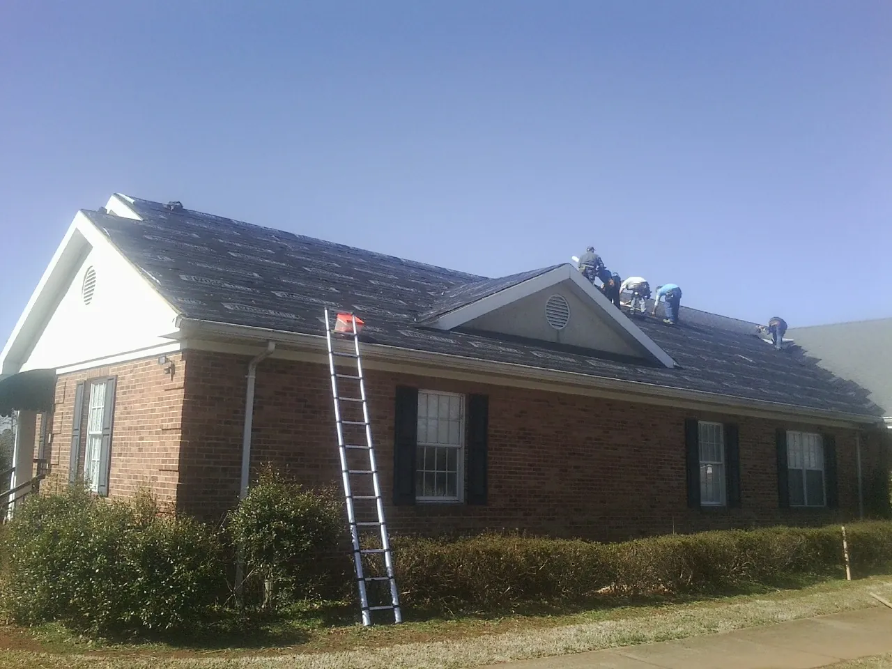 Crew tearing shingles off a brick ranch roof with a ladder set — Metal Roof Repair work by our crew in Huntingdon