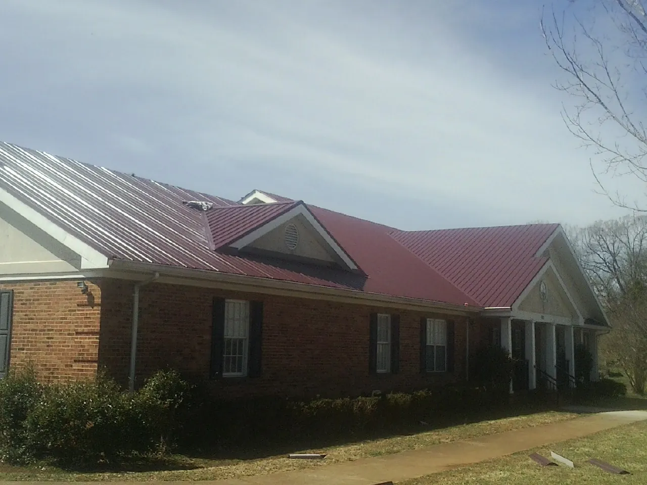 Red metal roof with gabled entries on a long brick building, from a Hail Damage Roof Repair job in Huntingdon