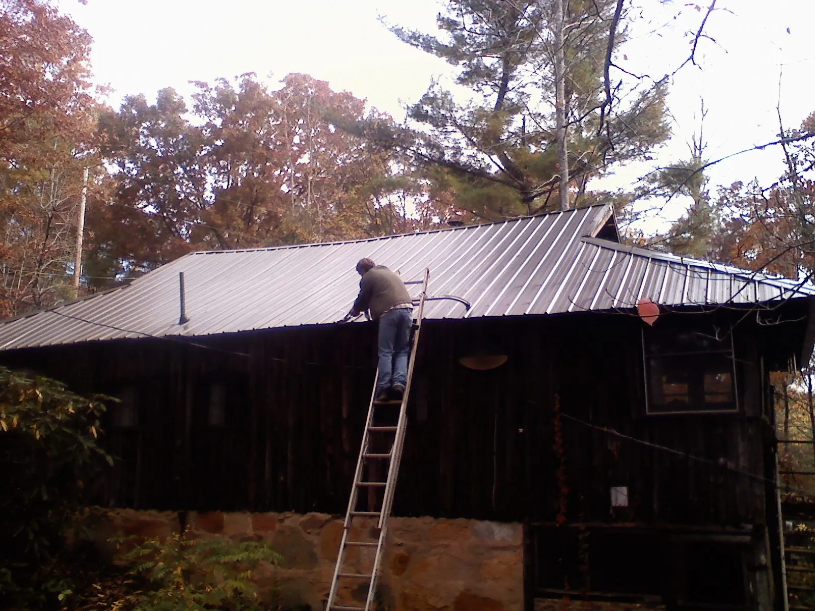 Roofer on a ladder working along the edge of a cabin metal roof in Huntingdon