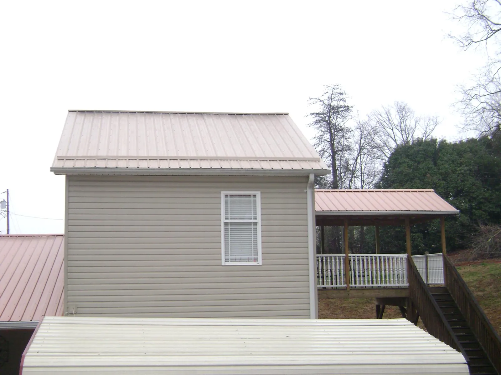 Tan metal roofs on a two story addition and attached porch, from a Roof Replacement job in Huntingdon